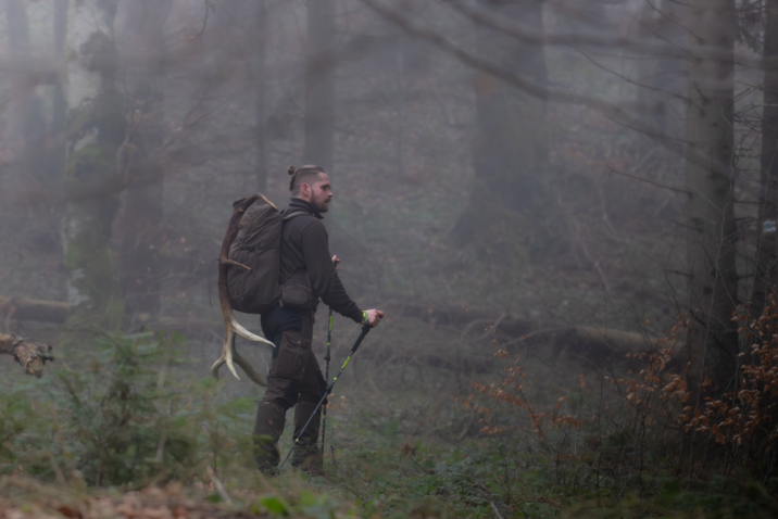 Zdjęcie przedstawia człowieka maszerującego po lesie z plecakiem, do którego ma przywiązane pojedynczą tykę z poroża jelenia. Fot. Daniel Pękalski